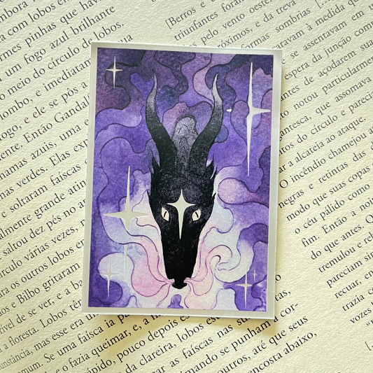 A rectangular art print featuring a stylized black dragon head with long horns on a purple and pink background, placed on top of an open book with printed text.